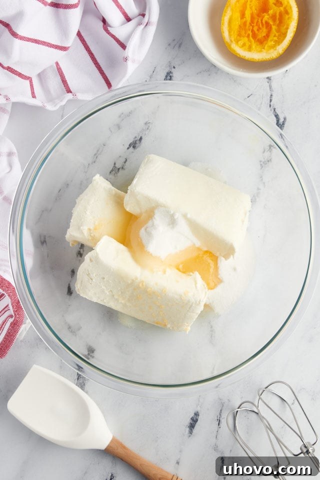 overhead view of cream cheese, sugar, and orange juice in a glass mixing bowl