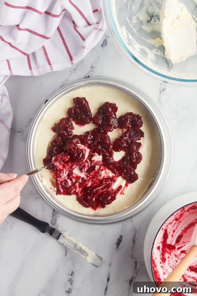 overhead view of the final layer of cranberry sauce being swirled into no-bake cranberry cheesecake