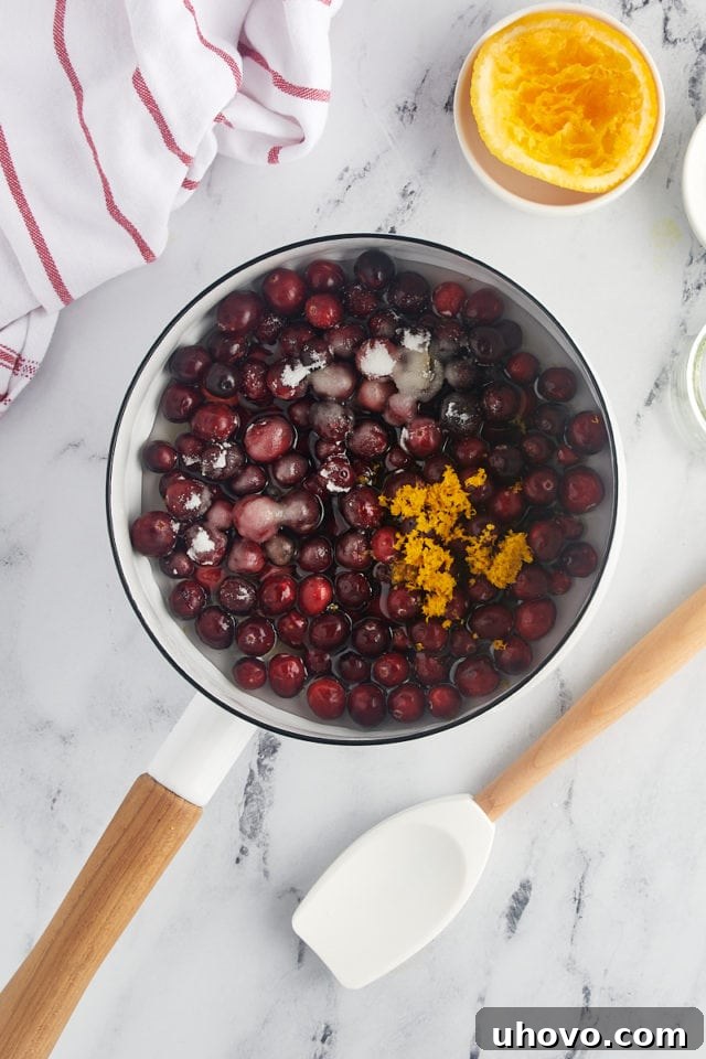 overhead view of cranberries, sugar, orange zest, orange juice, and water in a saucepan