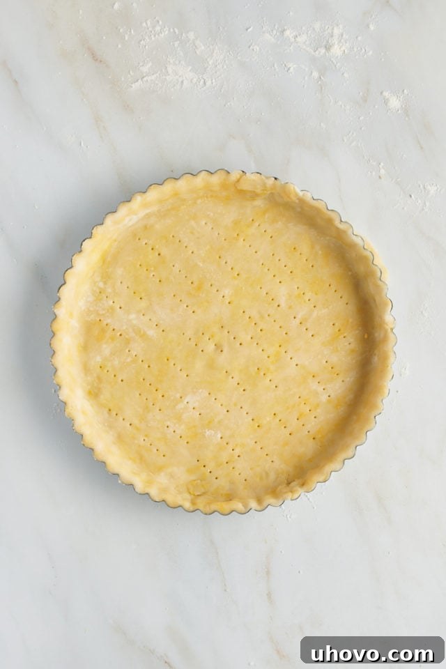 Overhead view of the pastry crust in the tart pan, with the bottom pricked thoroughly with a fork to prevent bubbling.