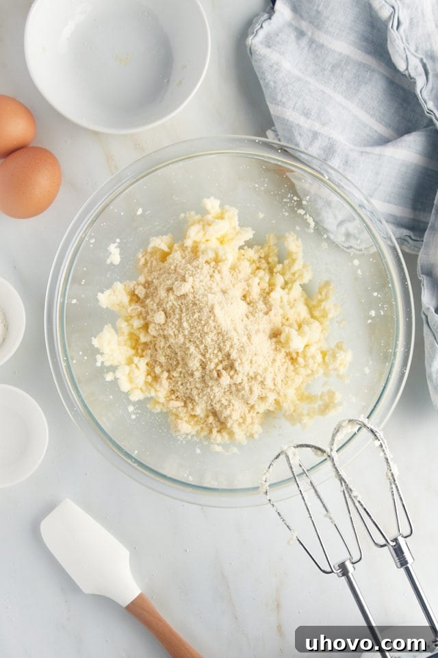Overhead view of creamed butter and sugar in a glass bowl, with almond flour just added and ready for mixing.