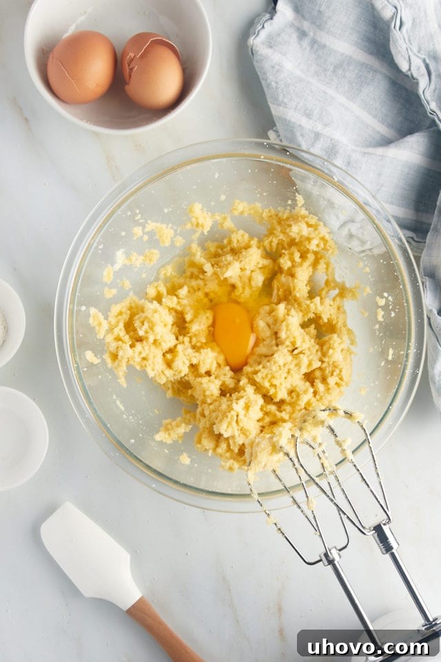 Overhead view of an egg being added to the creamy frangipane mixture in a glass bowl.