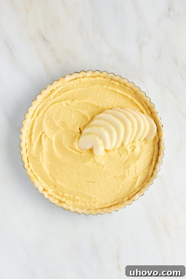 Overhead view showing the artistic process of arranging sliced pears concentrically on top of the frangipane filling in the tart.