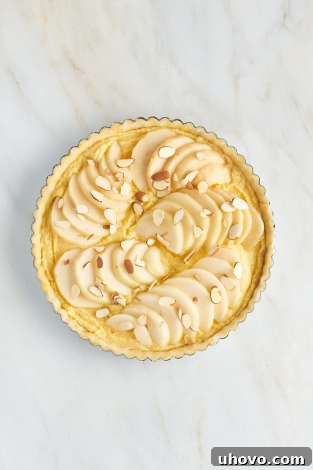 Overhead view of the complete pear frangipane tart, with pears and sliced almonds arranged, ready to be baked.