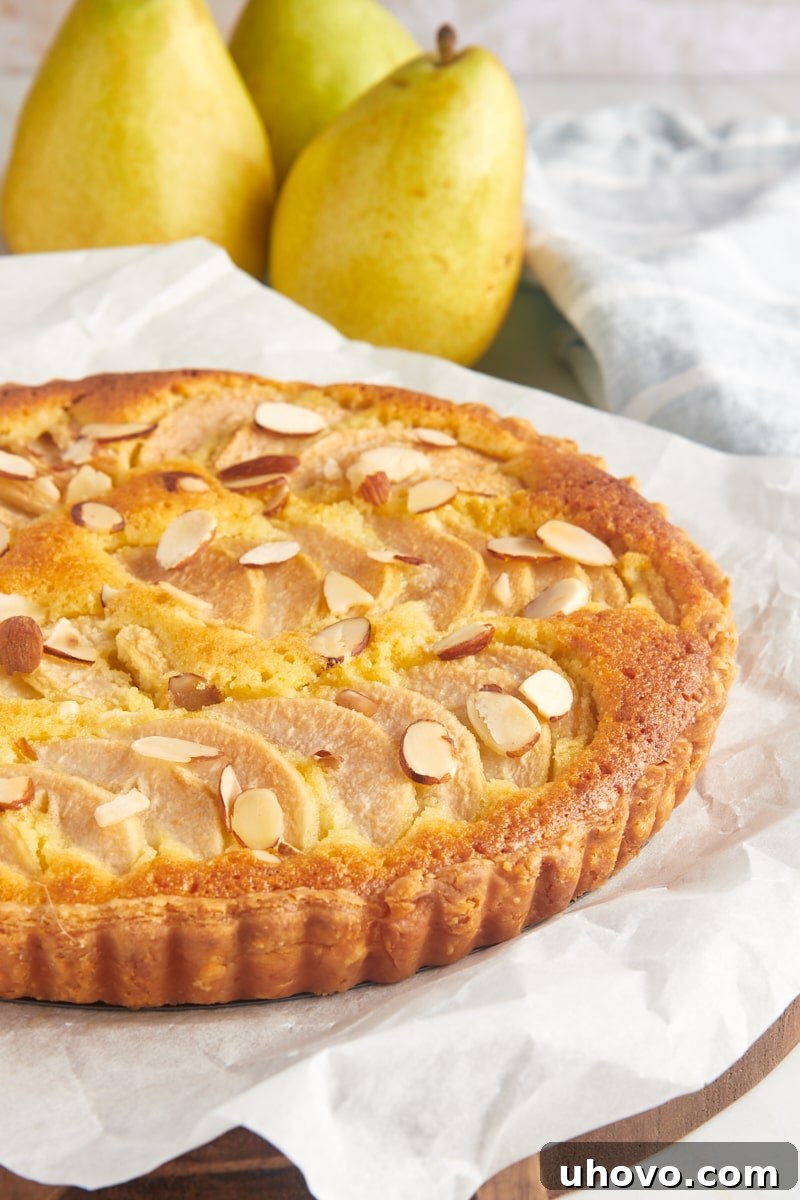 A whole baked pear frangipane tart artfully displayed on a parchment-lined wooden board, highlighting its golden crust and fanned pear topping.