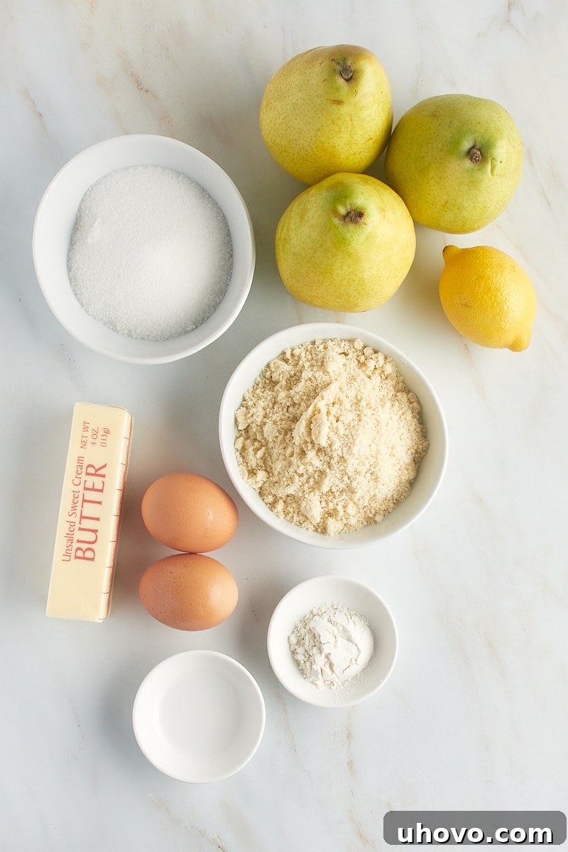 Overhead view of all ingredients for the pear frangipane tart filling, including pears, lemon juice, softened butter, granulated sugar, almond flour, eggs, and almond extract, neatly arranged in bowls.