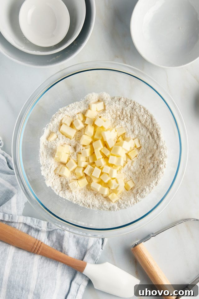 Overhead view of cold butter cubes being added to the dry ingredients for the tart dough in a glass bowl.