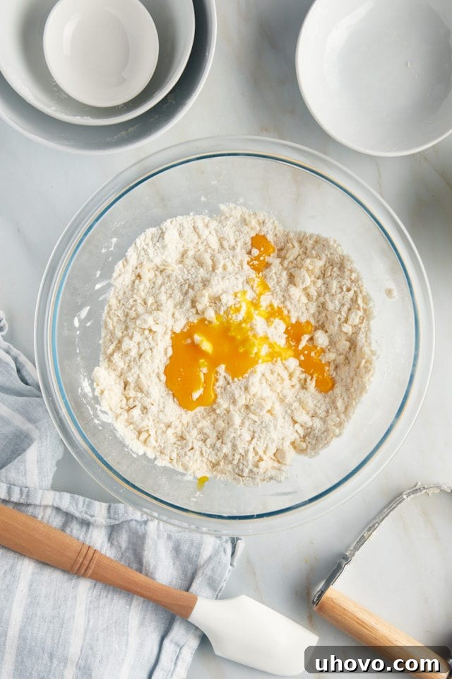 Overhead view of an egg yolk being added to the flour and butter mixture for the tart dough in a bowl.