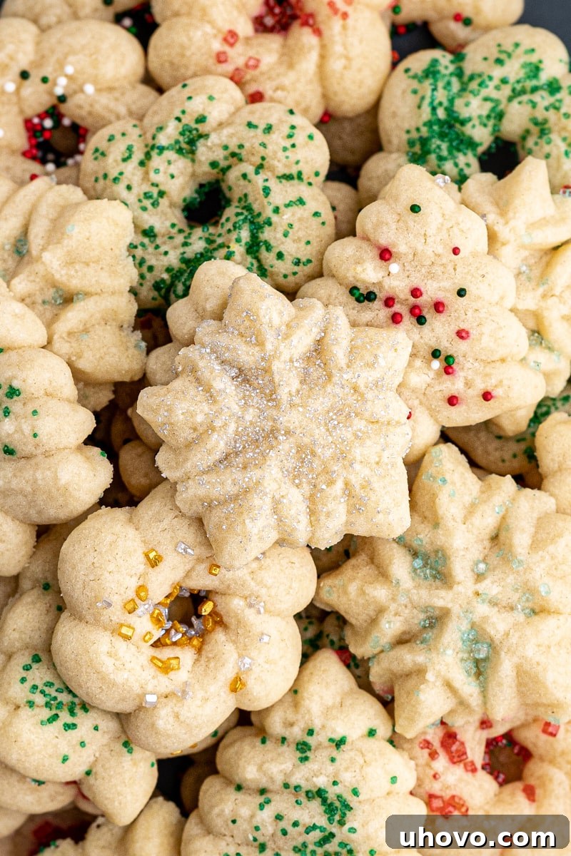 An overhead view of a large pile of colorful spritz cookies, decorated with red, green, gold, and silver sprinkles, evoking a festive and inviting atmosphere.