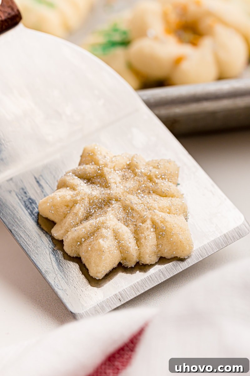 A delicate snowflake-shaped spritz cookie, perfectly baked and adorned, gently rests on a cookie spatula, ready to be served.