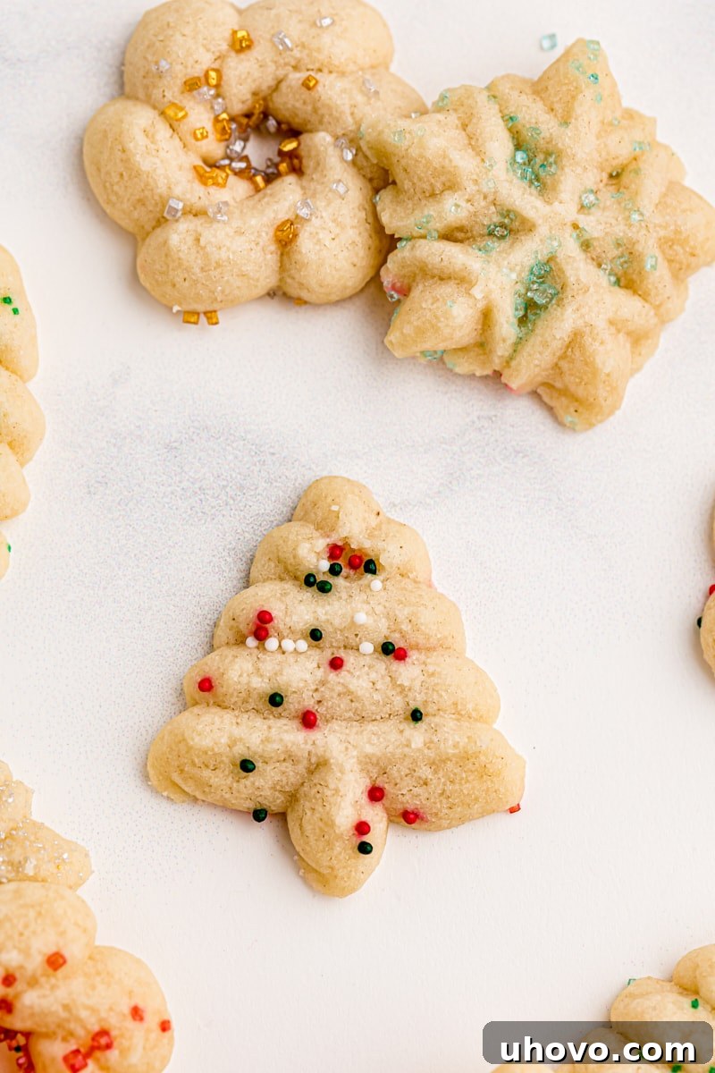 A beautifully shaped Christmas tree spritz cookie, adorned with festive sprinkles, is prominently displayed with other colorful spritz cookies surrounding it on a baking sheet.
