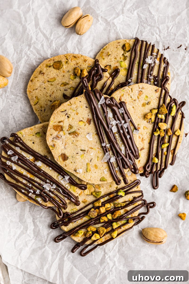 overhead view of a pile of chocolate-drizzled pistachio cookies on parchment paper