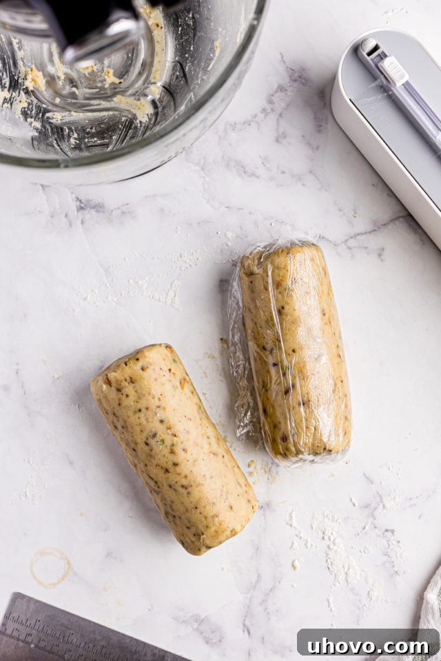 overhead view of two logs of pistachio cookie dough wrapped in plastic wrap