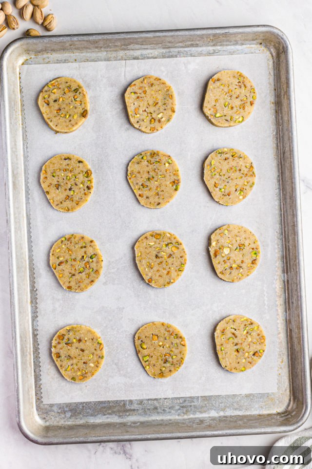 overhead view of sliced pistachio cookie dough on a parchment-lined baking sheet