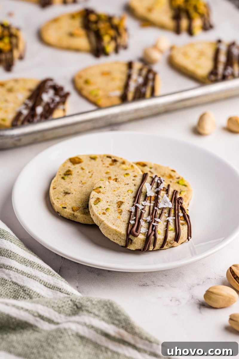 three pistachio cookies on a white plate with more cookies in the background