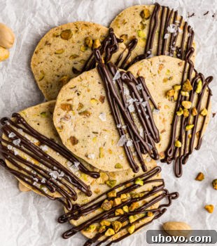 overhead view of a pile of chocolate-drizzled pistachio cookies on parchment paper