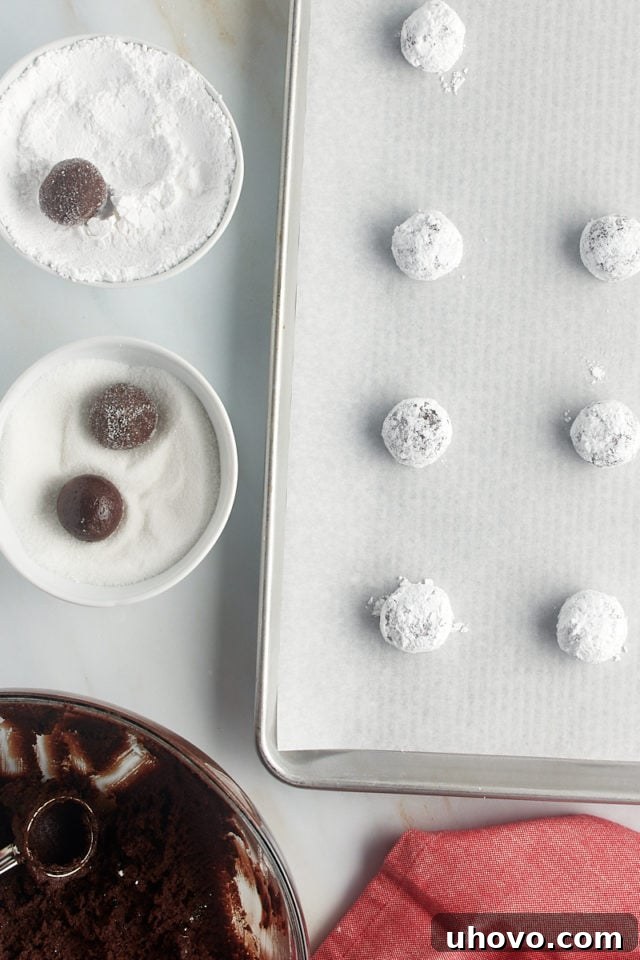 Overhead view of chocolate crinkle cookie dough in various stages of being rolled first in granulated sugar, then heavily in confectioners' sugar.