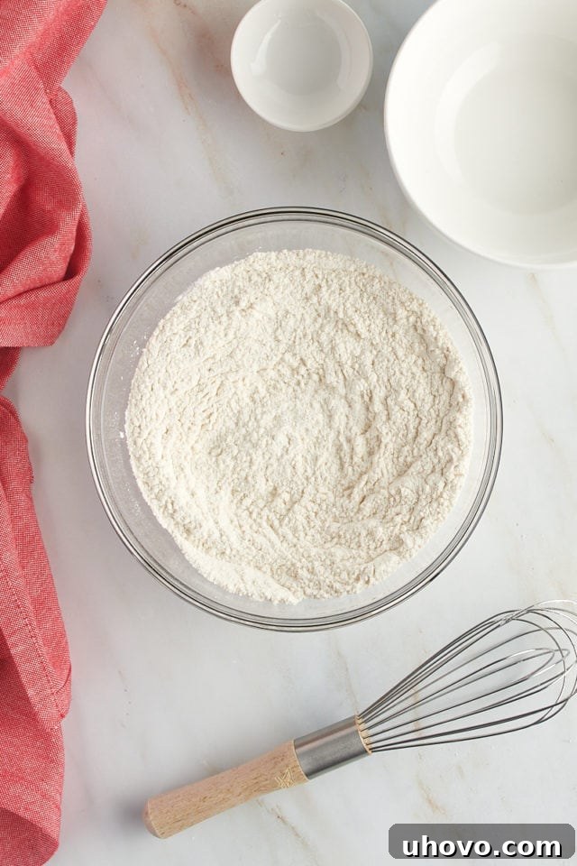Overhead view of all-purpose flour, baking powder, and salt mixed together in a clear glass bowl, ready for the next step.