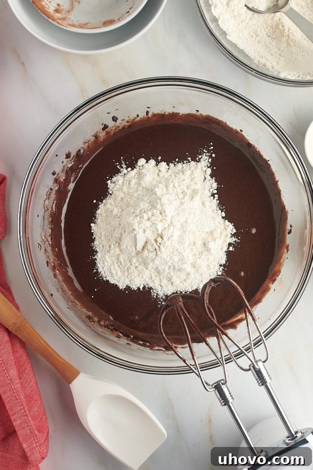 Overhead view of the flour mixture being gradually added to the chocolate crinkle cookie dough in a glass bowl.