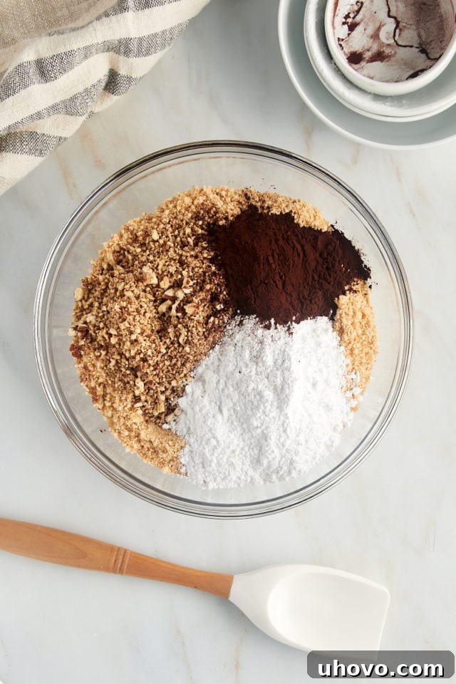 overhead view of vanilla wafer crumbs, chopped pecans, confectioners' sugar, and cocoa powder in a glass mixing bowl