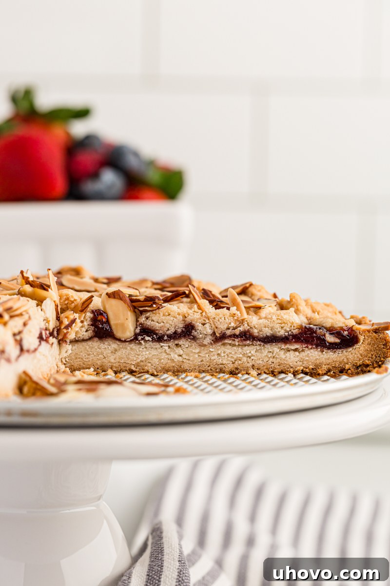 A partial view of a baked Italian Jam Crostata, artfully placed on a white cake stand, showcasing its inviting golden crust and textured topping.