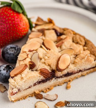 A delicious slice of Italian Jam Crostata on a white plate with fresh berries, inviting and perfectly baked.