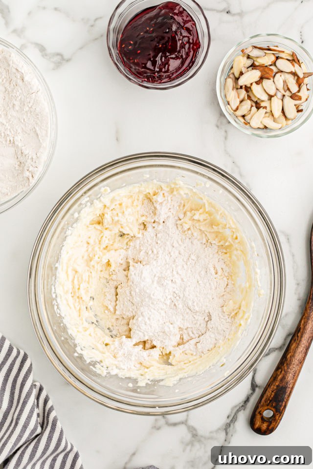 Overhead view of all-purpose flour being gradually added to the crostata dough mixture in a glass mixing bowl, showing the next stage of dough preparation.