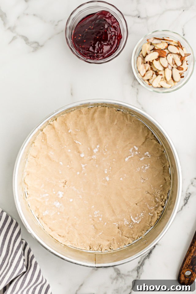 Overhead view of the crostata crust meticulously pressed into the bottom of a 10-inch springform pan, showing an even base ready for filling.