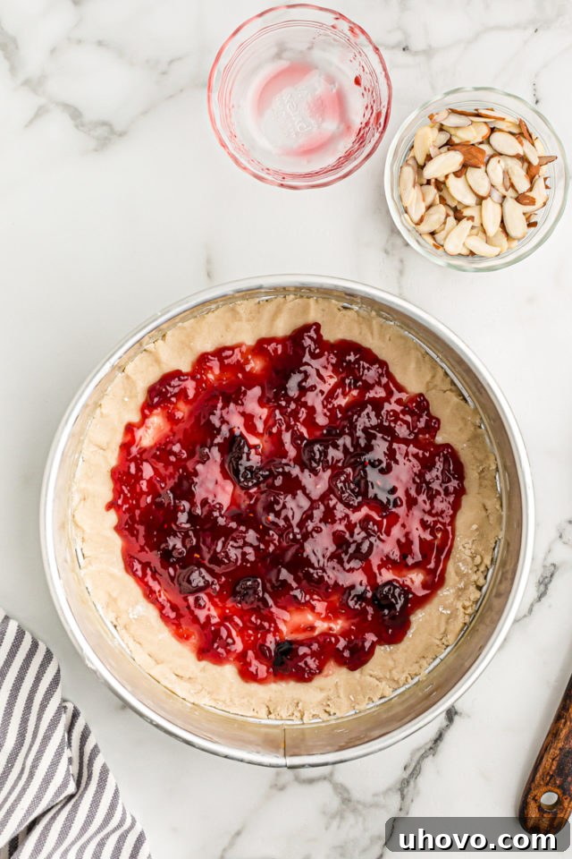 Overhead view of a vibrant layer of fruit jam evenly spread over the pressed crostata crust in a springform pan, leaving a slight border.