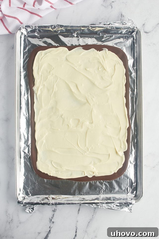 Overhead view of two distinct chocolate layers, dark and white, for peppermint bark, with the white layer fully spread.
