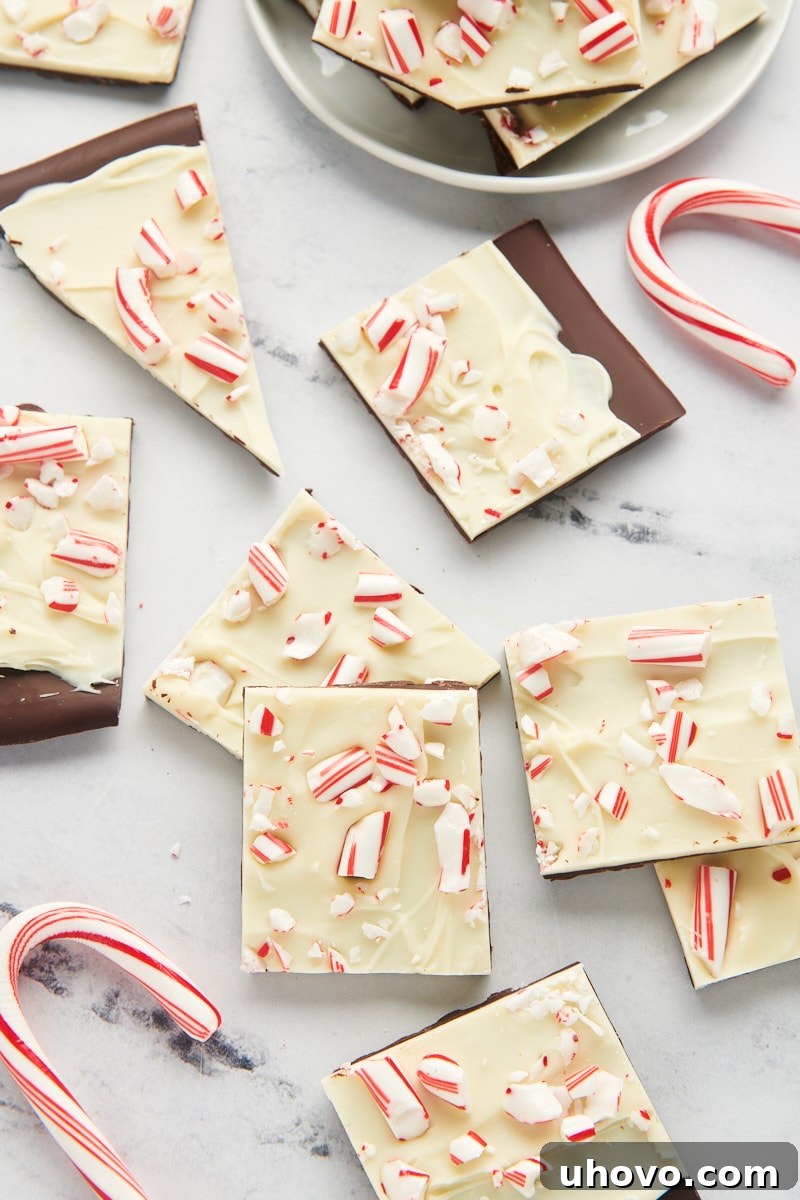 Peppermint bark pieces and several festive candy canes are artfully scattered across a clean marble countertop, creating a holiday scene.