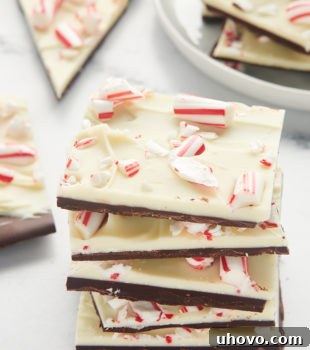 Five pieces of peppermint bark stacked together with more bark in the background, signaling a festive treat.