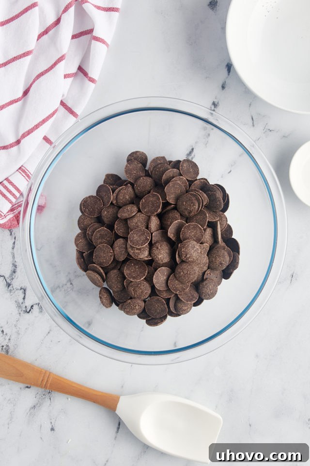 Overhead view of dark chocolate discs placed in a clear glass mixing bowl, ready for melting.
