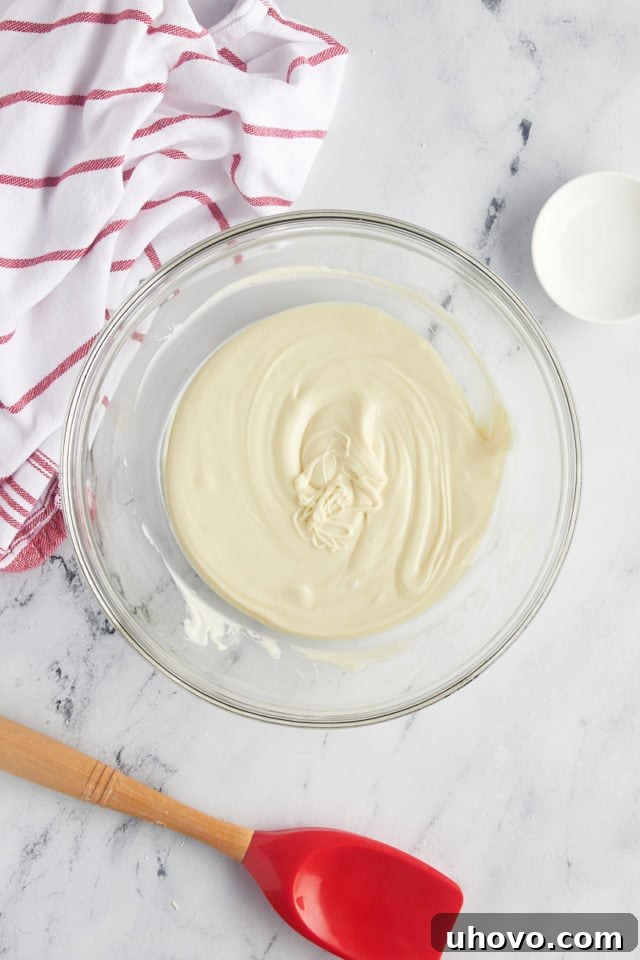 Overhead view of silky smooth melted white chocolate in a glass mixing bowl, ready for the next step.