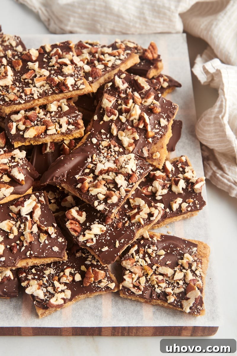 Pile of golden Graham Cracker Toffee on a parchment-lined wooden board, highlighting its crunchy texture and chocolate-nut topping.