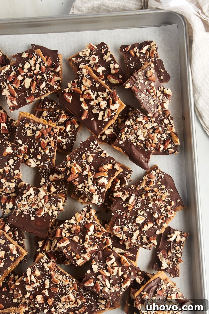 Overhead view of numerous pieces of Graham Cracker Toffee scattered on a parchment-lined baking sheet, showcasing their distinct layers.
