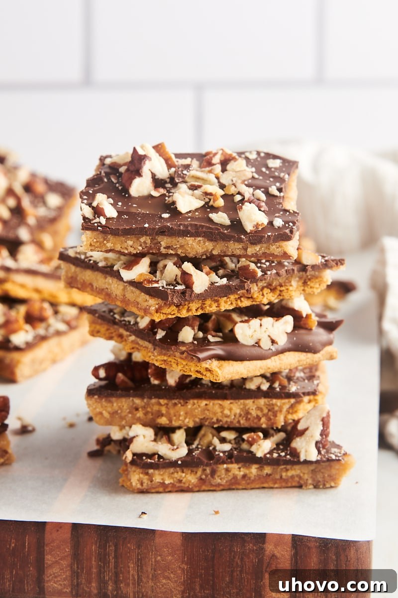 A stack of five perfectly broken pieces of Graham Cracker Toffee, with more toffee blurred in the background, showing off its inviting layers.
