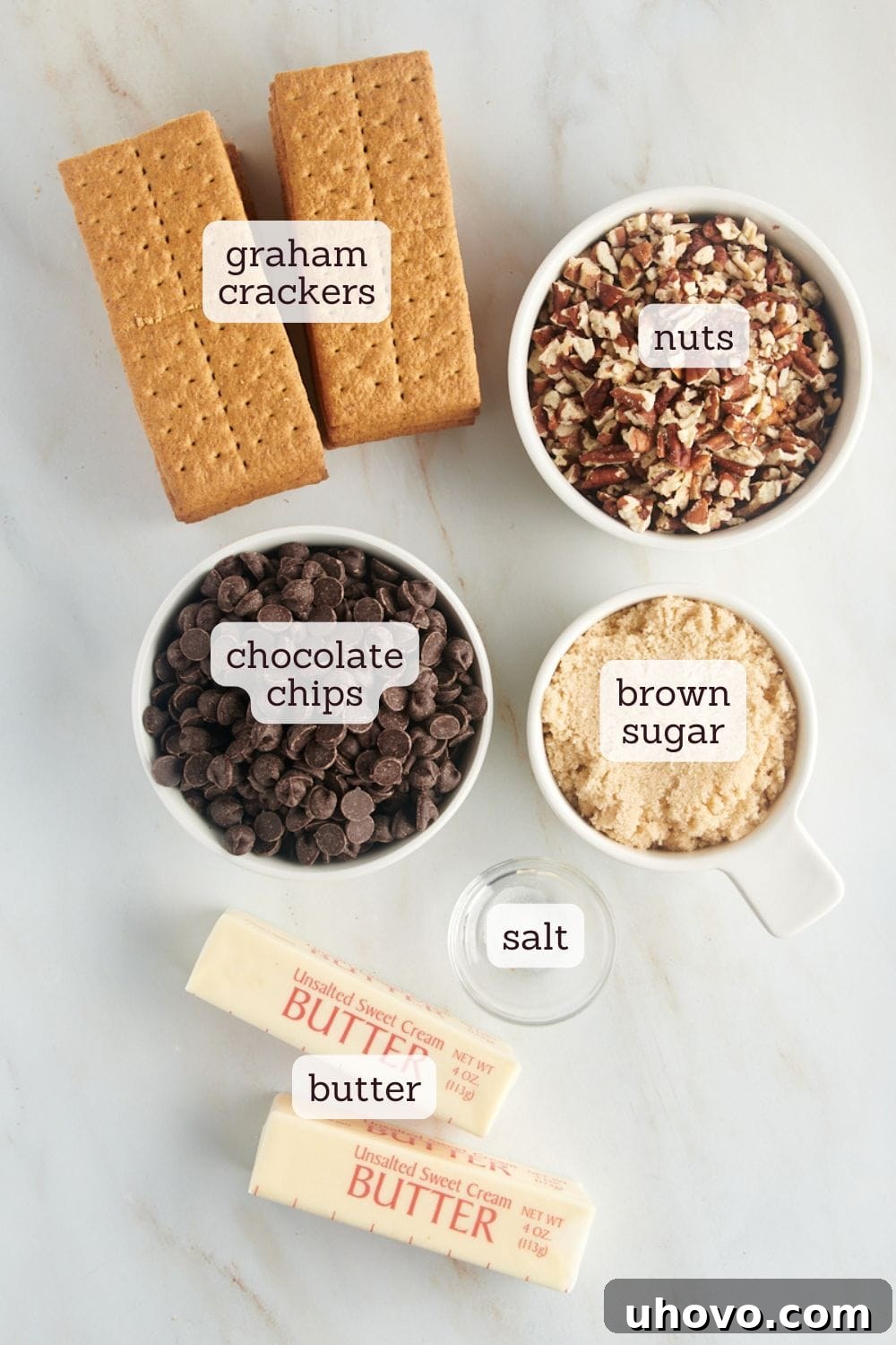 Overhead view of all ingredients for Graham Cracker Toffee laid out on a clean surface: graham crackers, butter, brown sugar, chocolate chips, and chopped pecans.