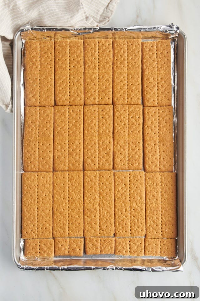 Overhead view of a single layer of graham crackers neatly arranged in a foil-lined half sheet pan.