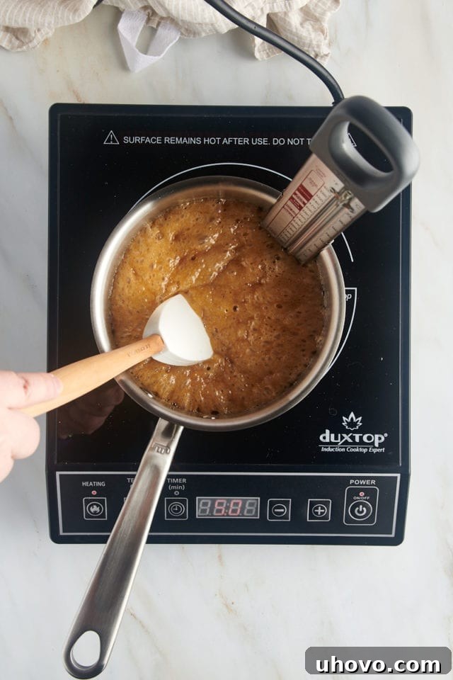 Overhead view of the butter and brown sugar mixture in a saucepan, having reached the soft crack stage, indicated by a candy thermometer.