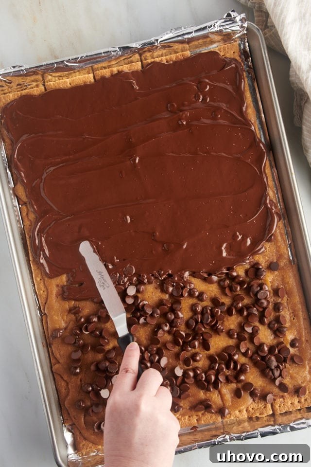 Overhead view of melted chocolate being smoothly spread across the baked graham cracker toffee layer.