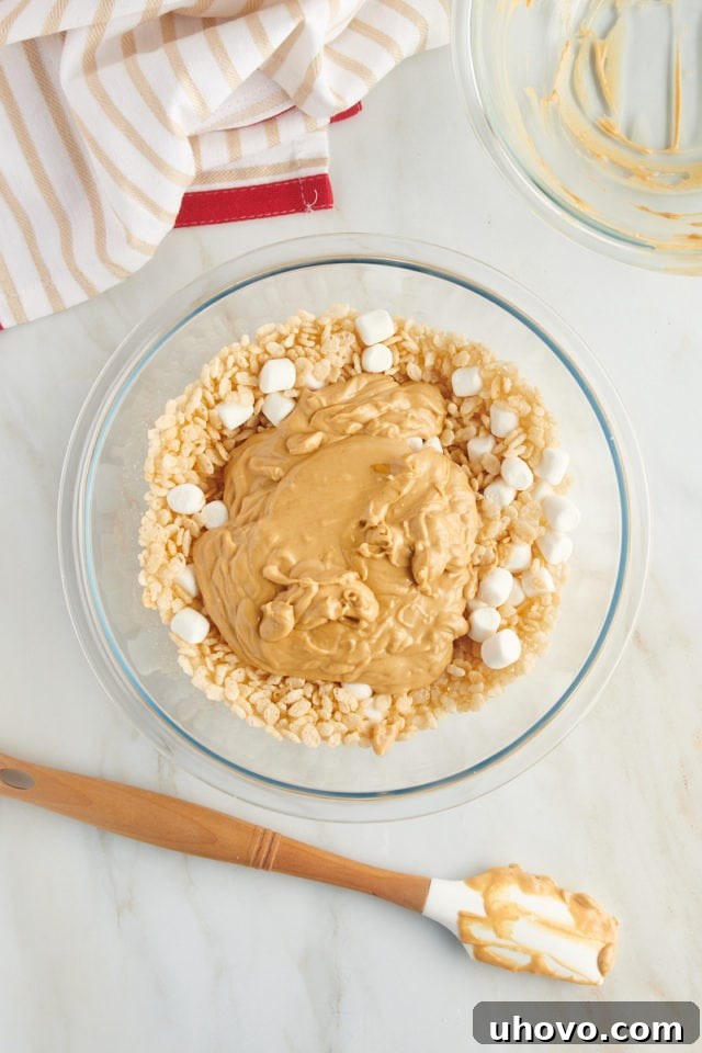 overhead view of melted white chocolate and peanut butter added to rice cereal and marshmallows in a glass bowl