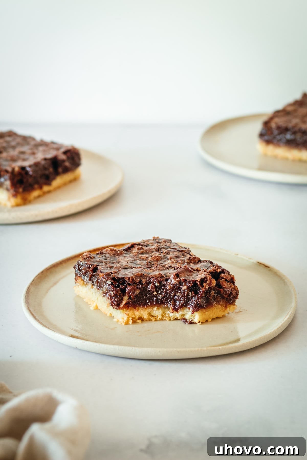 Three plates of chocolate pecan pie bars, with one having a bite taken out