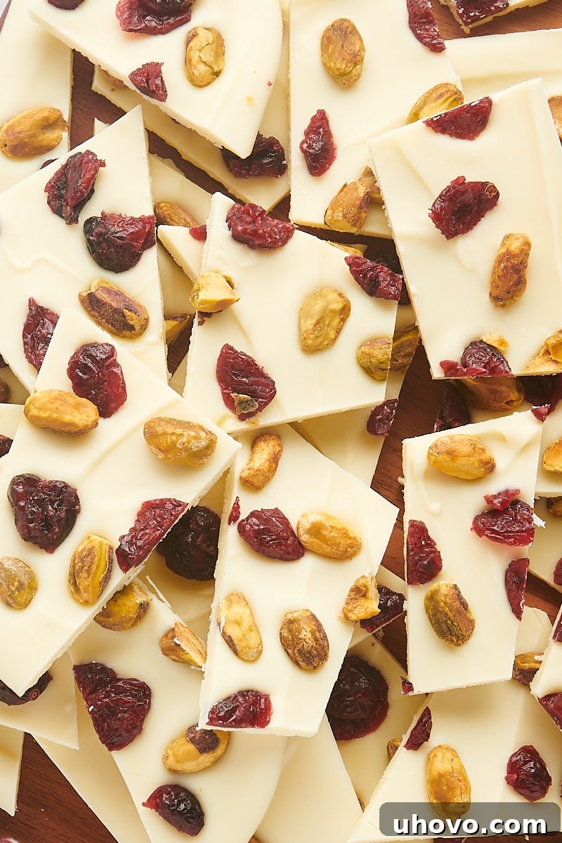 overhead view of cranberry pistachio bark pieces piled on a wooden board, showcasing vibrant red cranberries and green pistachios against white chocolate