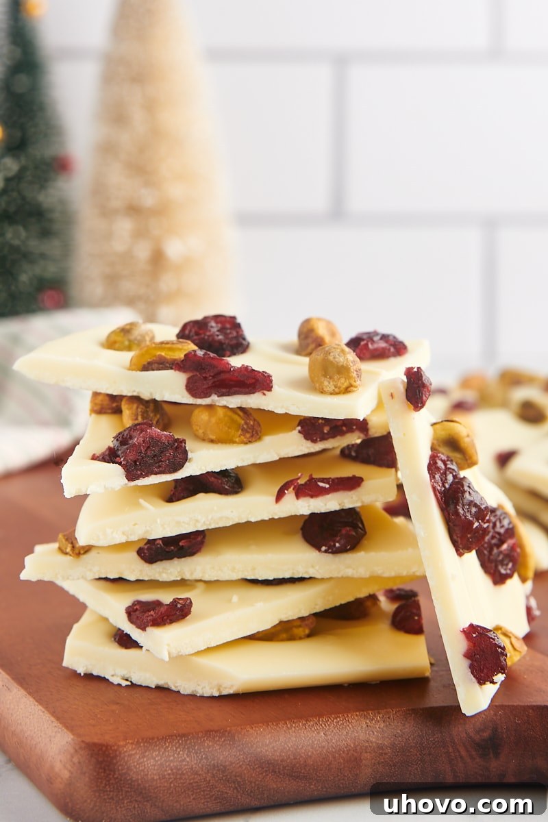 several pieces of cranberry pistachio bark artfully stacked on a wooden cutting board, showing off the varying textures and colors