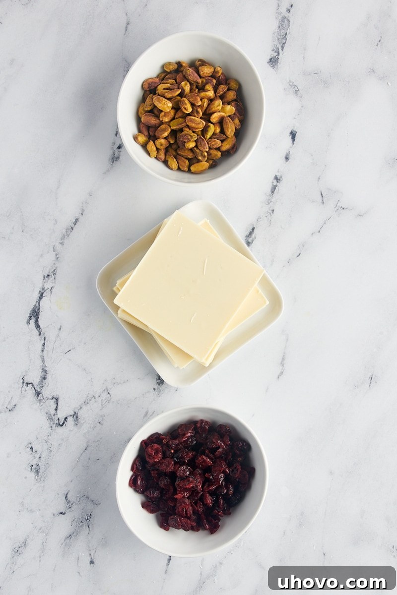 overhead view of ingredients for cranberry pistachio bark laid out on a clean surface: white chocolate, dried cranberries, and shelled pistachios