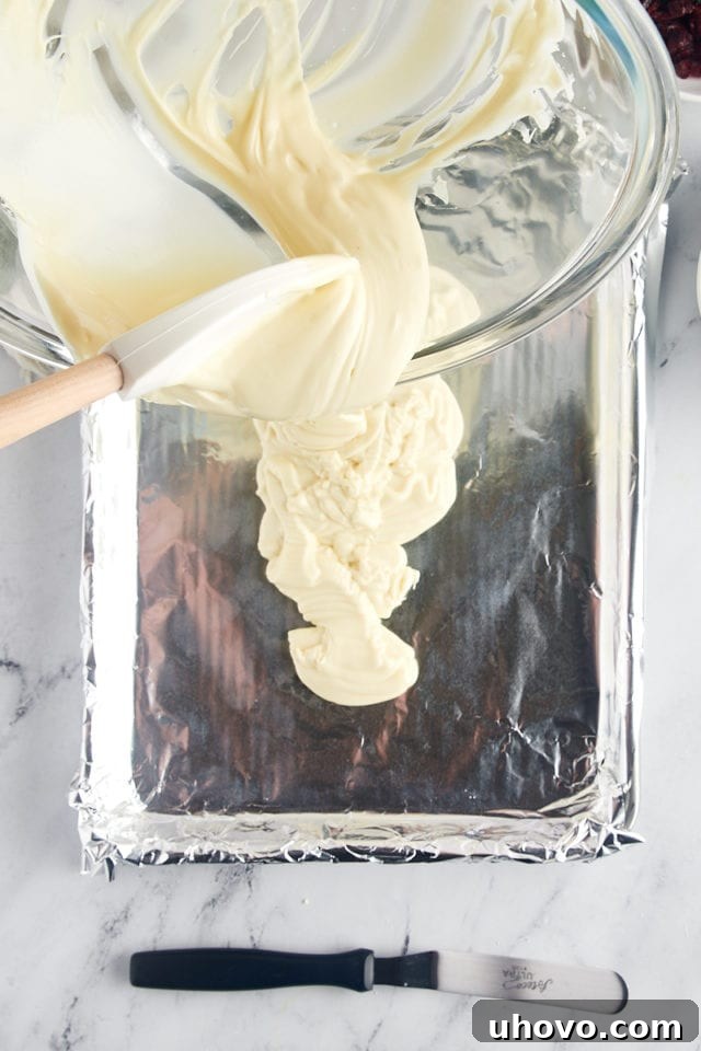 overhead view of melted white chocolate being carefully poured onto a foil-lined baking sheet