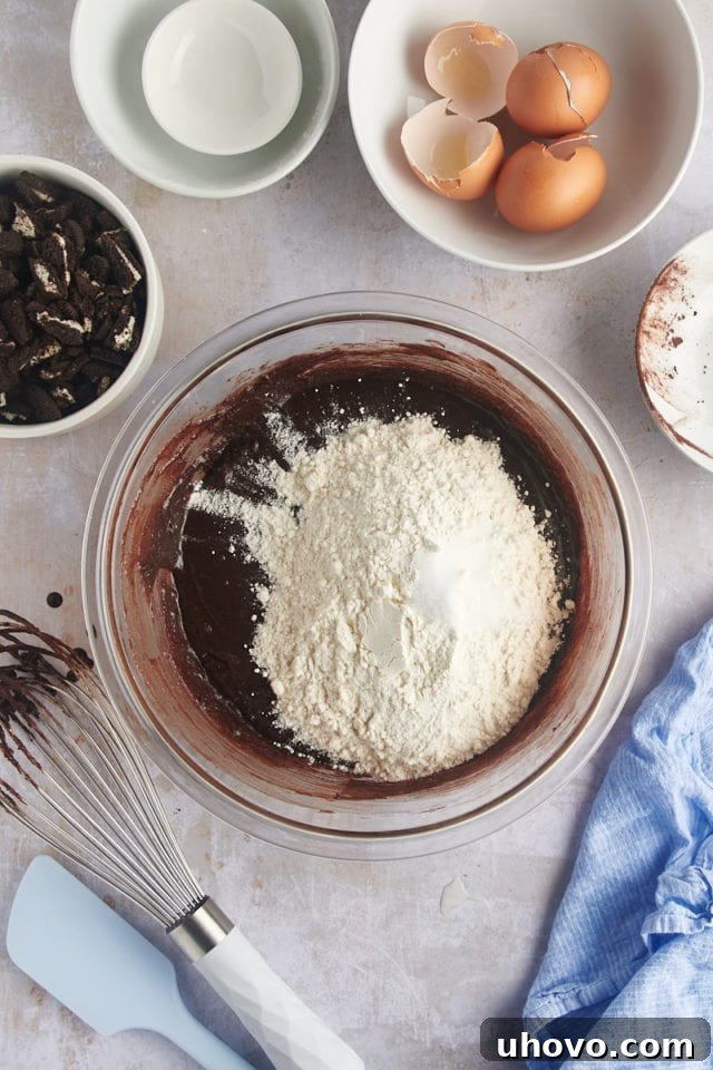 Overhead view of flour and salt being added to the liquid ingredients, forming the brownie batter.