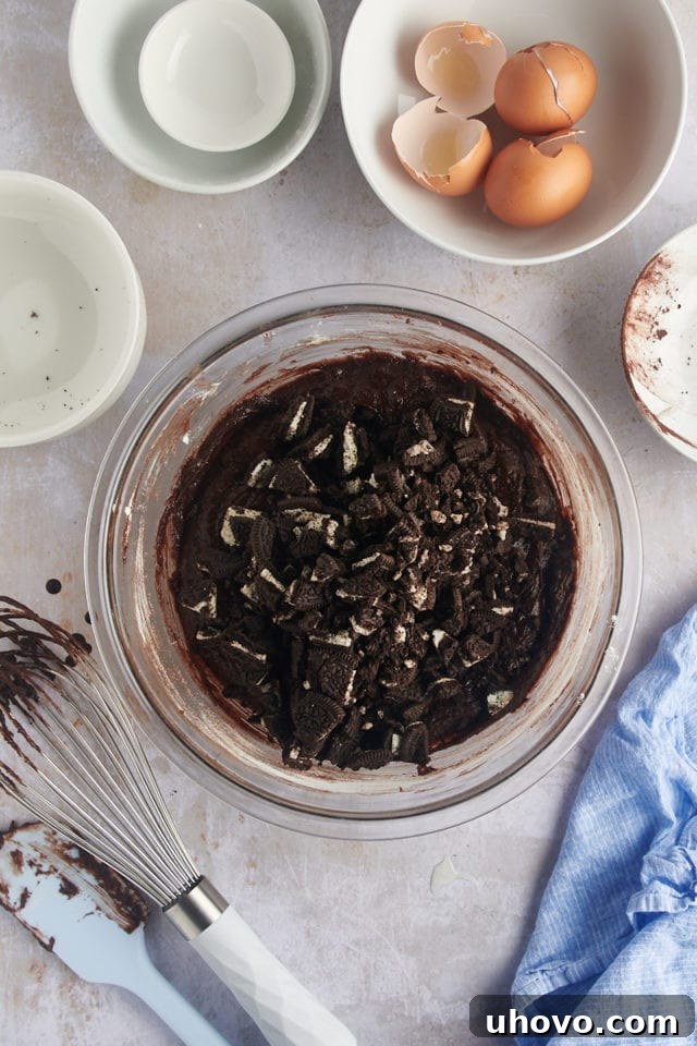 Overhead view of crushed Oreo pieces being folded into the rich brownie batter in a mixing bowl.
