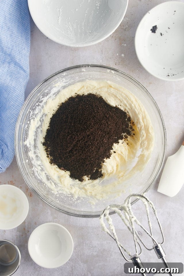 Overhead view of finely crushed Oreo crumbs being added to the creamy frosting mixture.
